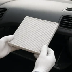 Hands installing a pleated cabin air filter into an open glove box compartment of a mid-size sedan