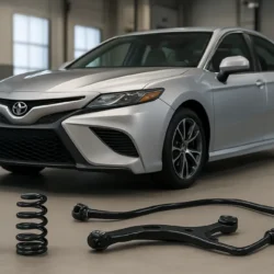 Toyota Camry with suspension components laid out on a workshop floor, including a shock, coil spring, control arm, and sway bar.